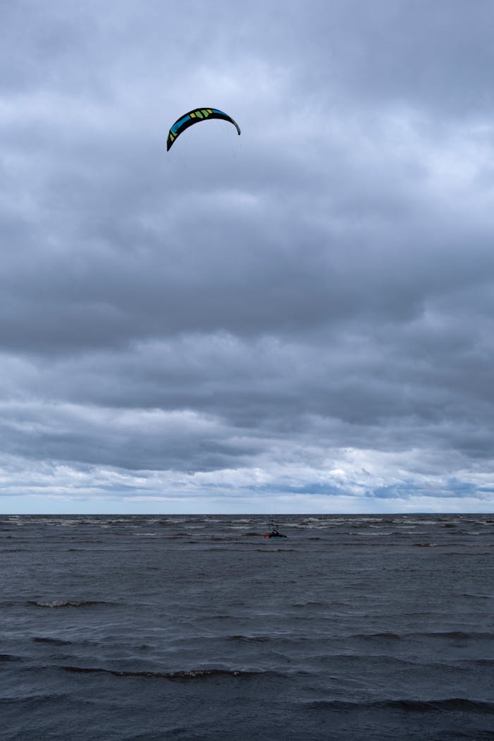 A kitesurfer harnesses the wind under overcast skies on a choppy sea.